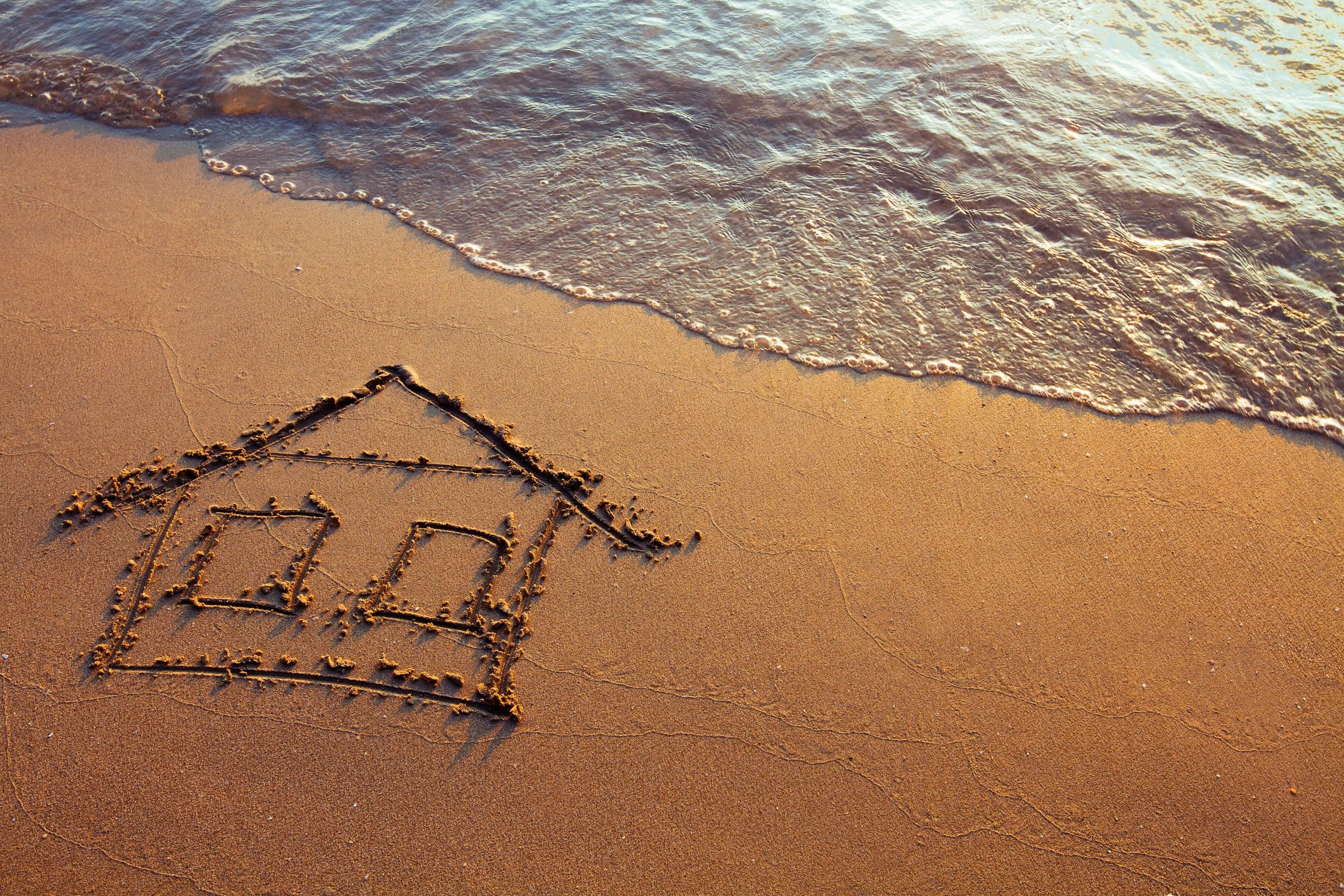 House drawn in sand with waves on shore